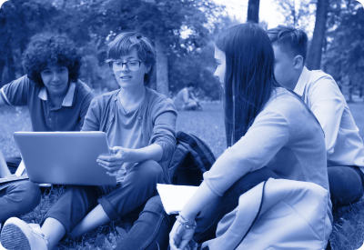 Czworo młodych ludzi siedzi na trawie w parku z otwartym laptopem, obraz w tonacji niebieskiej