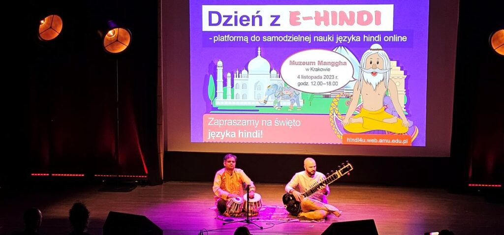 A big slide with a caption "A day with ehindi", a drawing of Taj Mahal and a sitting yogi. In front of it two musicians are sitting and playing Indian instruments. 