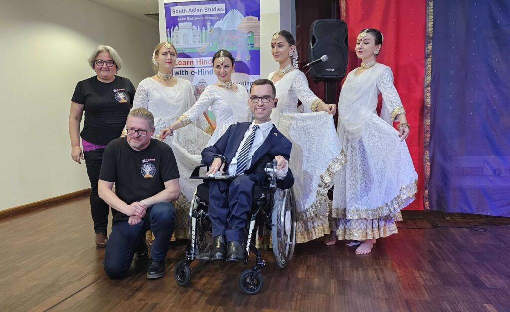 From the left: Monika Browarczyk, Krzysztof Stroński, Adrian Furman. Behind them, four dancers in white long dresses, in the background a poster promoting eHindi